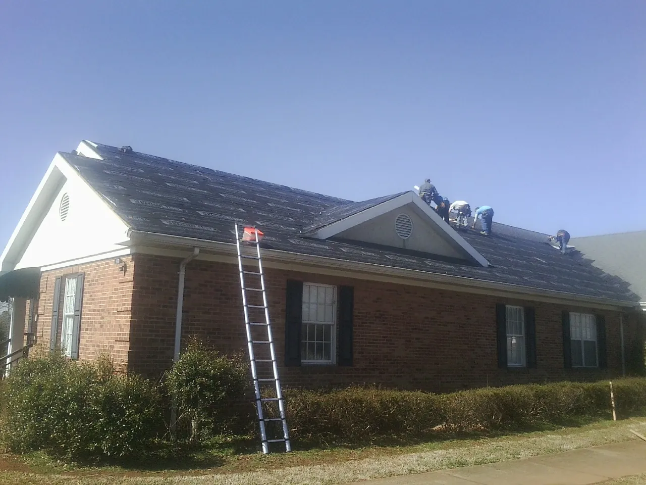 Crew tearing shingles off a brick ranch roof with a ladder set — Metal Roof Repair work by our crew in Venango