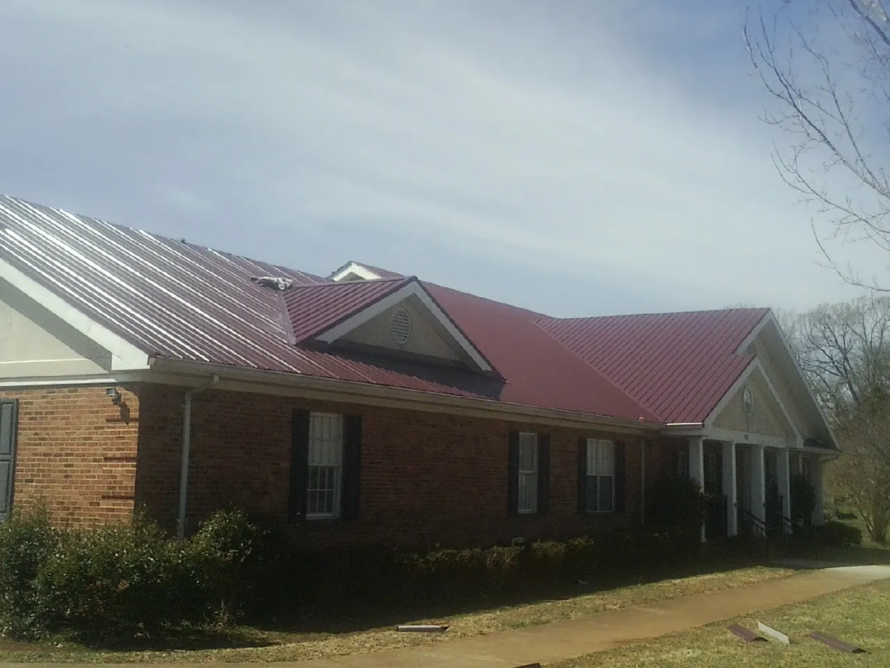Red metal roof with gabled entries on a long brick building, from a Hail Damage Roof Repair job in Venango