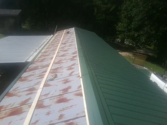 Old rusted panels beside newly installed green metal roofing — Wind Damage Roof Repair by Roofing Brothers in Venango