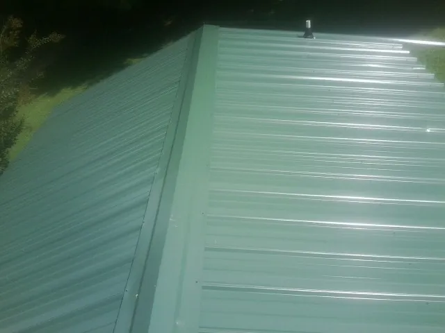 New green metal panels meeting at the ridge of a roof — Flat Roof Repair work by our crew in Venango